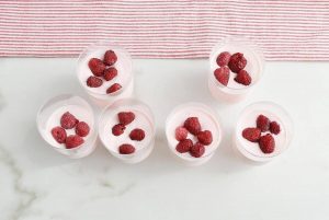 6 Greek Yoghurt and Raspberry Jelly cups sitting on a marble table.